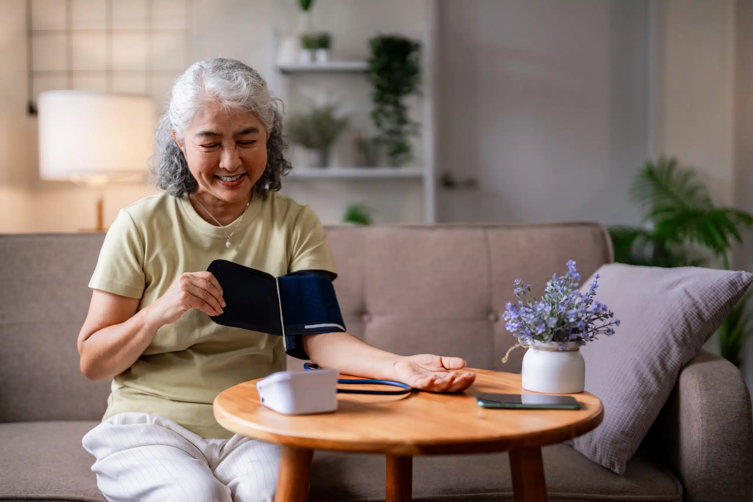 What To Do Before and After an IME Appointment 2 Joyful senior Asian lady actively checks vital signs using a personal blood pressure monitor. Proactive health management and comfortable home wellness.
