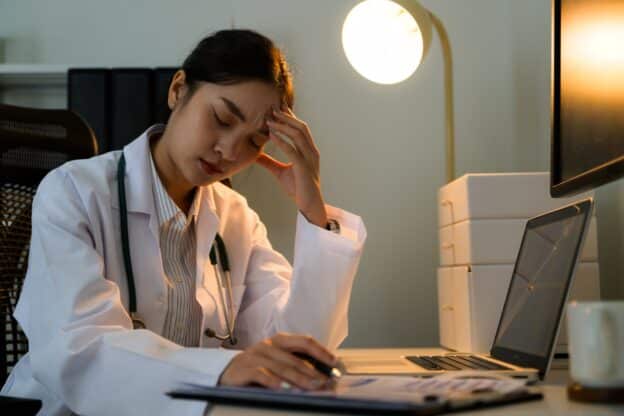 Exhausted female doctor holding head while reviewing medical records late at night