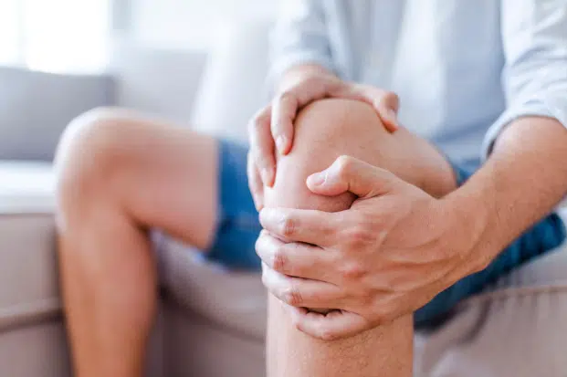 How Can I Get Short- or Long-Term Disability for Knee Pain? 2 A close-up of a person sitting and holding their knee with both hands, indicating pain or discomfort in the joint.
