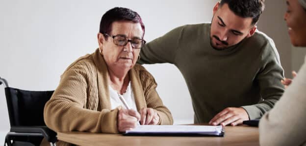 An older woman filling out paperwork with a person giving guidance