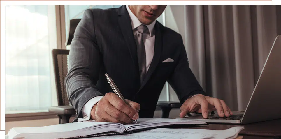 Long-Term Disability Benefits 6 Attorney in a dark suit signing legal documents at a desk while working on a laptop in a modern office setting.