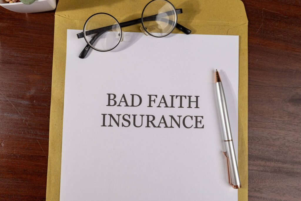 Document labeled "Bad Faith Insurance" on a manila envelope with round-frame glasses and a silver pen on a wooden desk