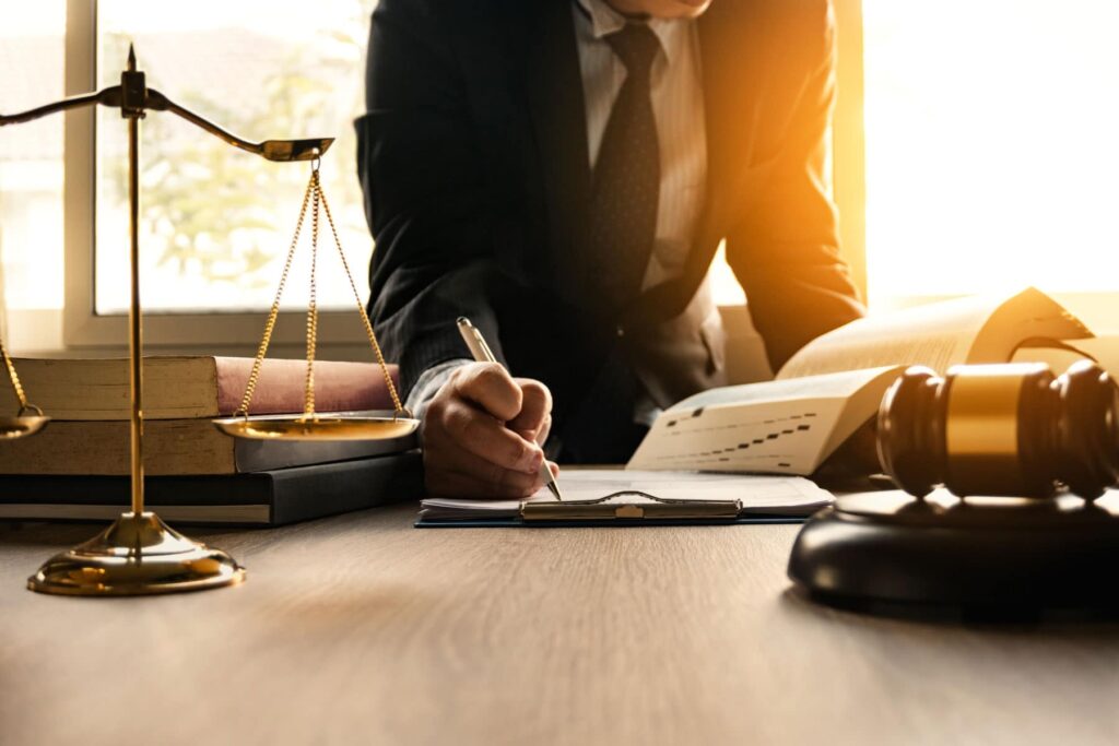 Attorney in a suit writing legal documents at a desk with a gavel, scales of justice, and law books nearby