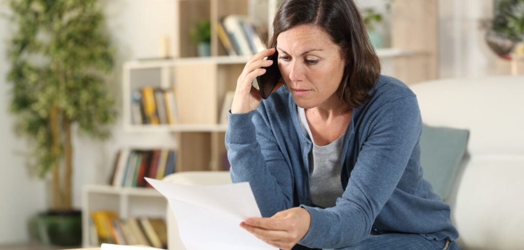 Concerned woman reviewing legal documents while speaking on phone at home