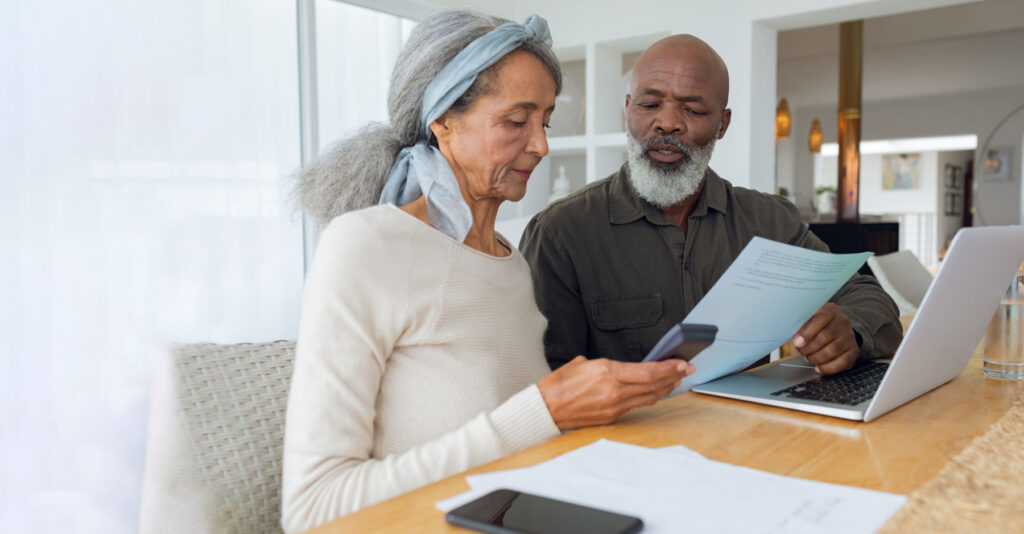 Older couple reviewing legal documents together at a home table with a laptop, discussing important paperwork