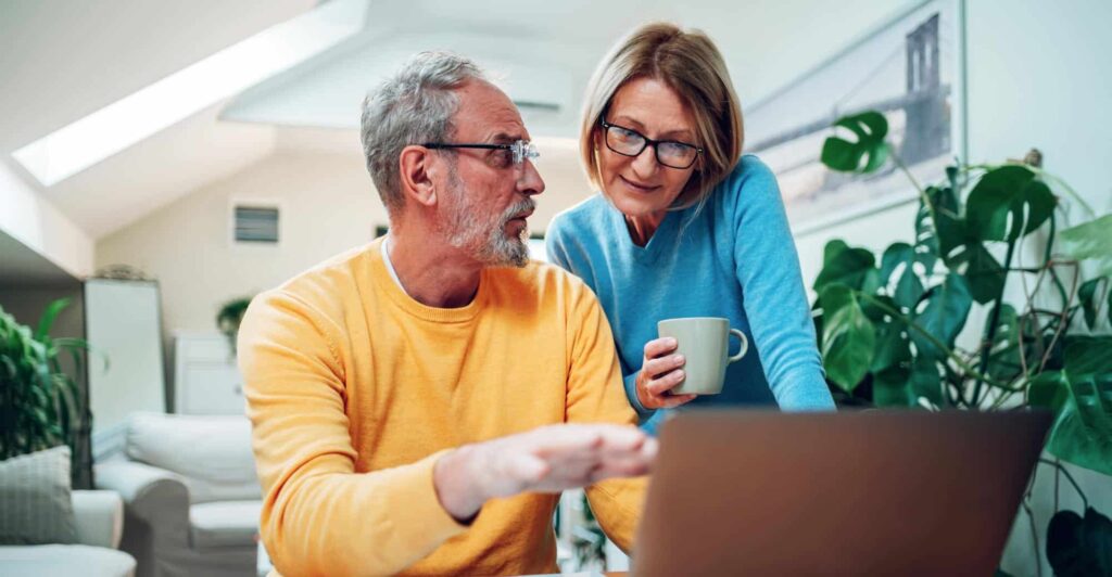 Middle-aged couple reviewing information on a laptop at home, discussing legal options together over coffee