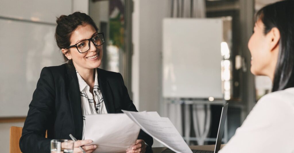 Female attorney in glasses smiling while reviewing legal documents with a client during a consultation meeting