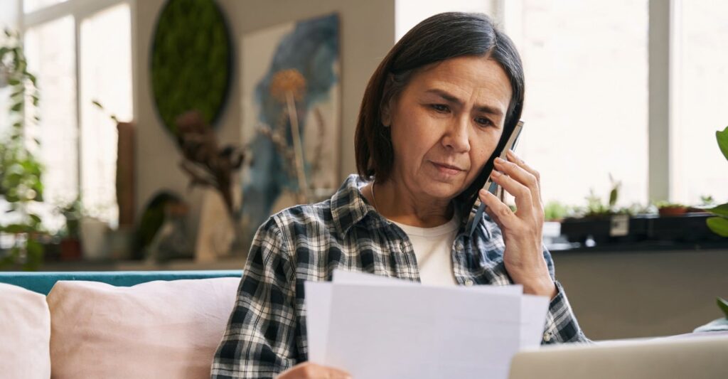 Concerned middle-aged woman reviewing legal documents while speaking on phone at home
