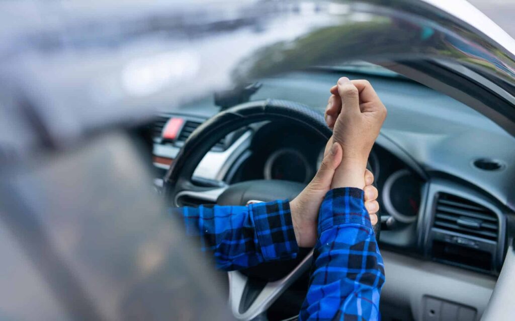 Driver in a blue plaid shirt holding their wrist in pain near the steering wheel, indicating a car accident injury