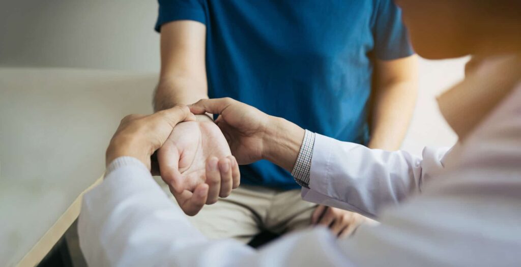 Doctor in white coat examining a patient's wrist and hand during a medical consultation for a potential injury