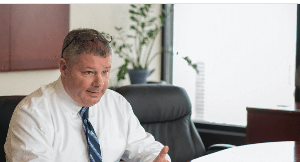 Attorney in white shirt and tie seated at office desk, reviewing documents in a professional law office setting