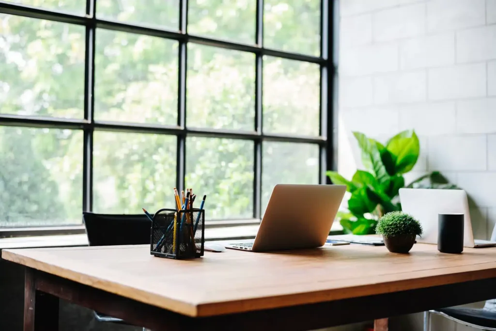 Modern law office desk with open laptop, pencil holder, and green plants beside a large window overlooking trees