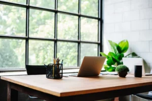 Modern law office desk with open laptop, pencil holder, and green plants beside a large window overlooking trees