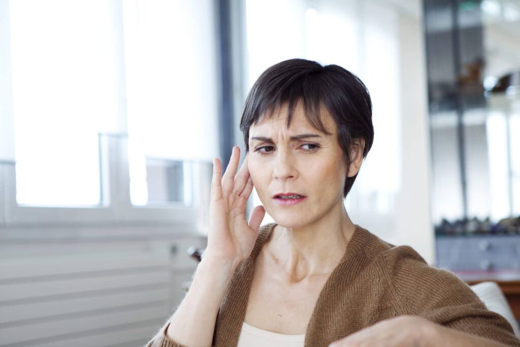 Woman with a concerned expression holding her hand to her face, appearing distressed or in pain indoors