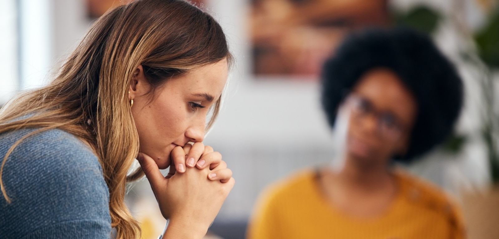 Distressed woman with clasped hands in a consultation, with a blurred advisor listening attentively in the background