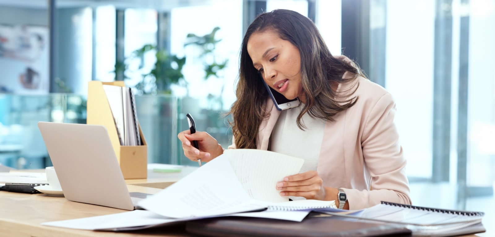 Female attorney reviewing legal documents while on a phone call at her office desk with a laptop nearby