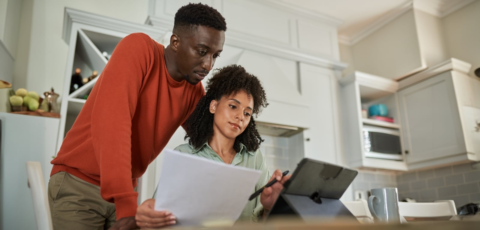 Couple reviewing legal documents and a tablet together at a kitchen counter, discussing important paperwork at home