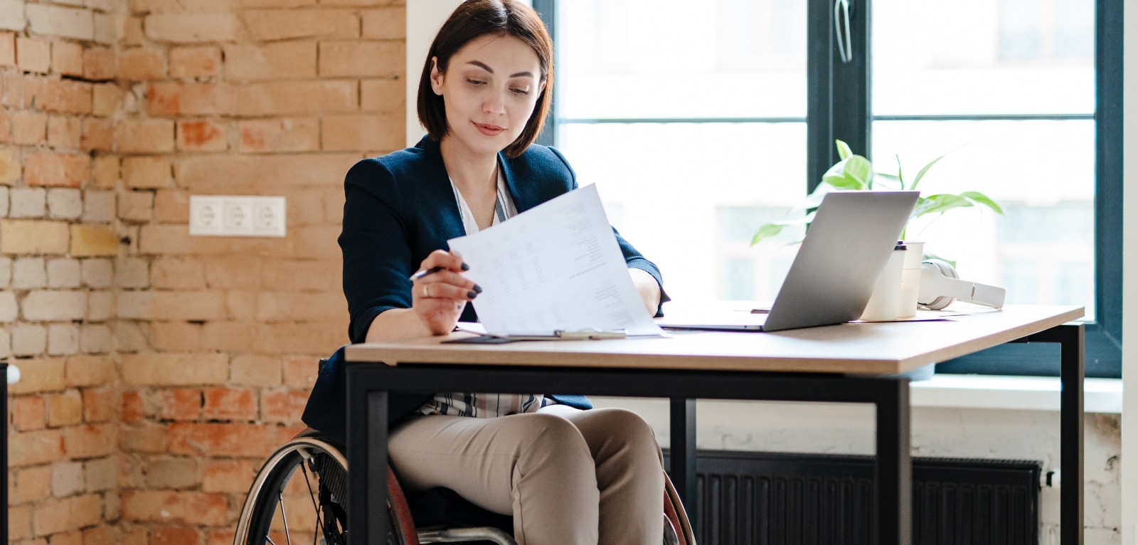 Woman in a wheelchair reviewing legal documents at a desk with a laptop in a modern office setting