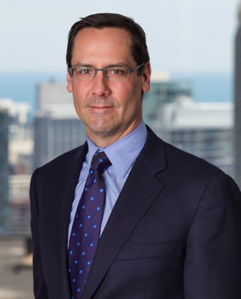 Male attorney in navy suit and tie with city skyline background, professional headshot