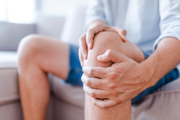 Person clutching their knee in pain while seated, indicating a knee injury or joint discomfort