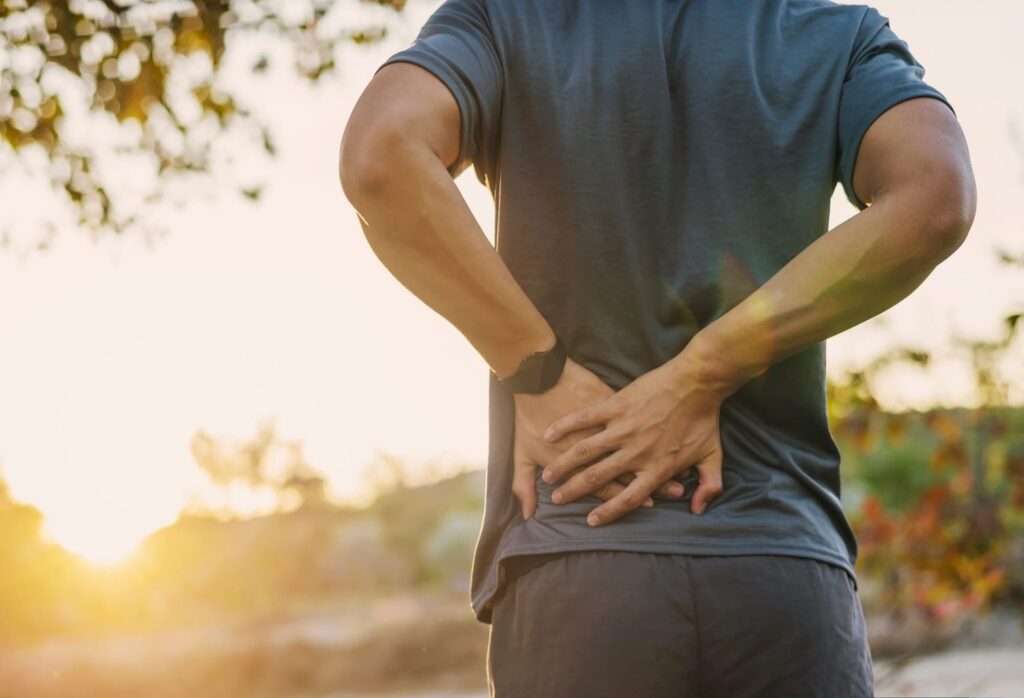 Man in athletic wear clutching his lower back in pain outdoors, depicting a common personal injury symptom