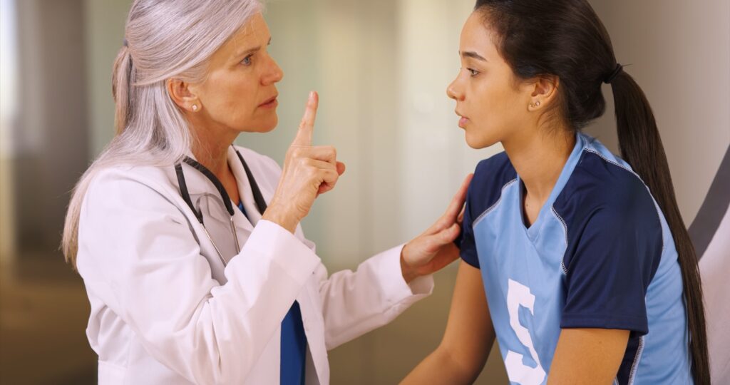 Doctor performing concussion assessment on young female athlete in sports jersey, using finger-tracking test