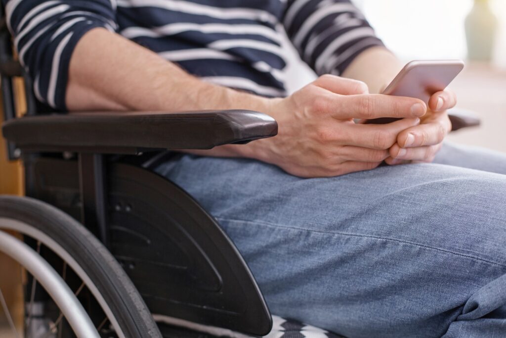 Person in a wheelchair using a smartphone, wearing a striped shirt and jeans, seeking legal assistance