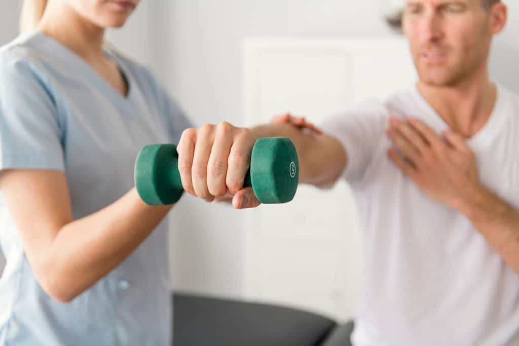 Physical therapist guiding a patient through dumbbell rehabilitation exercises during injury recovery treatment session