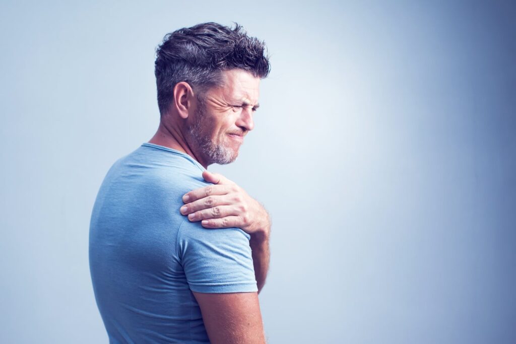 Middle-aged man grimacing in pain while gripping his shoulder, representing personal injury suffering and physical trauma