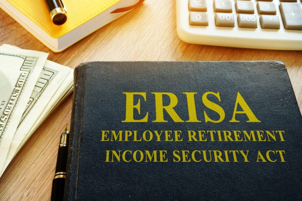 ERISA Employee Retirement Income Security Act binder on a desk with cash, pen, notebook, and calculator
