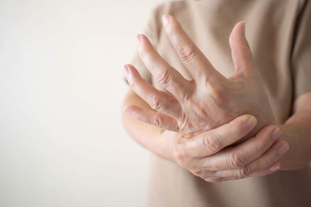 Elderly person clutching their hand in pain, showing signs of arthritis or joint discomfort in fingers and wrist