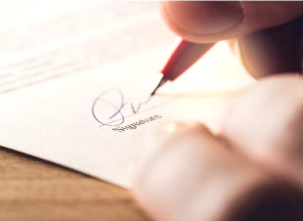 Person signing a legal document with a red pen on the signature line of an official contract