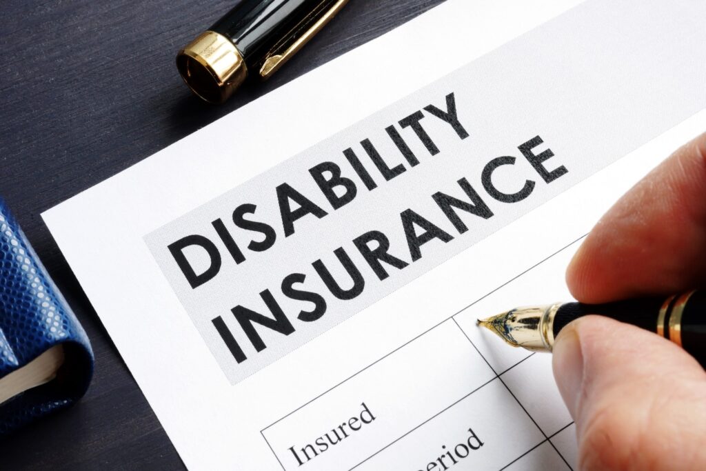 Person signing a disability insurance claim form with a fountain pen on a dark desk