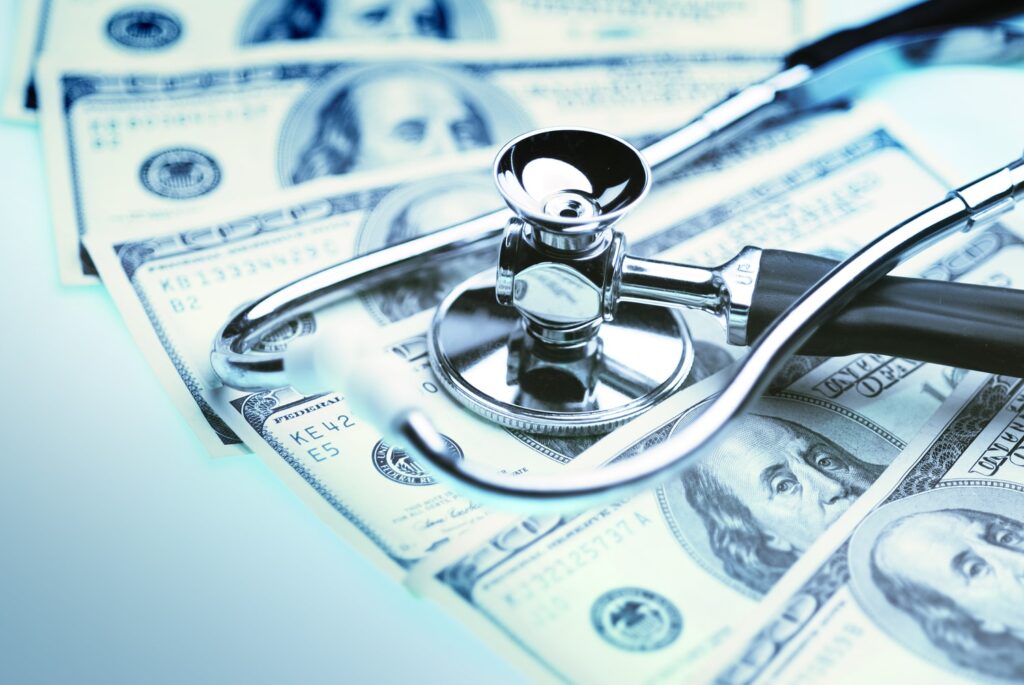 Stethoscope resting on spread US hundred-dollar bills, representing medical costs and personal injury compensation