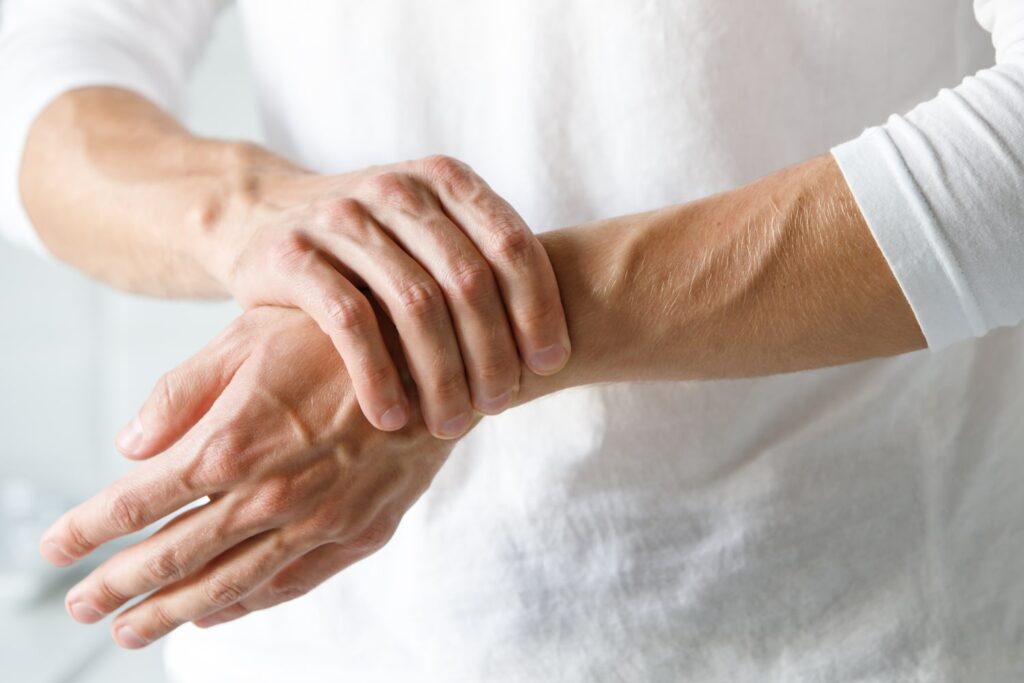 Person in white shirt clutching their wrist in pain, indicating a wrist injury or repetitive stress condition