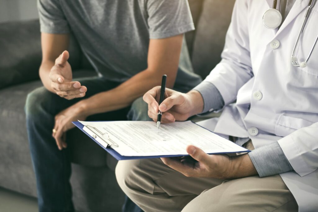 Doctor with stethoscope writing on clipboard during patient consultation, reviewing medical records or treatment notes