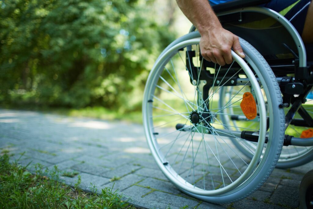 Person in a wheelchair gripping the wheel while navigating an outdoor paved path surrounded by green trees