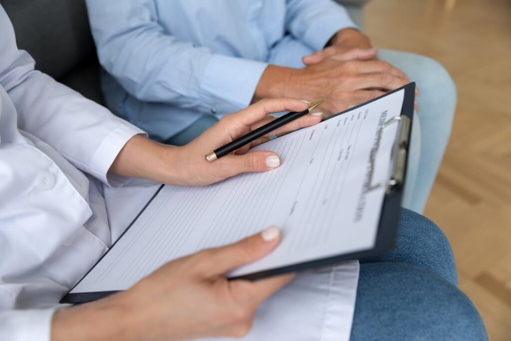 Healthcare professional in white coat holding clipboard with medical form and pen during patient consultation
