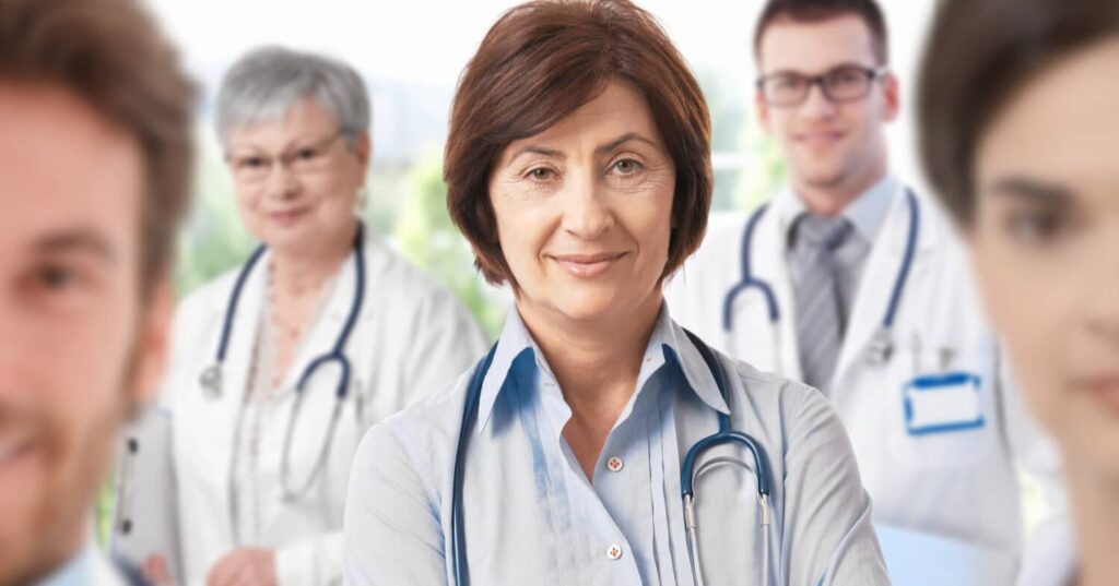 Female physician with stethoscope standing confidently in front of a team of medical professionals in white coats