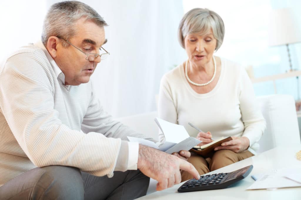 Elderly couple reviewing financial documents and using a calculator at home, discussing bills or legal paperwork together