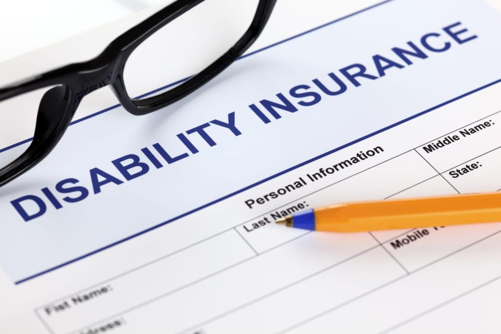 Disability insurance claim form with personal information fields, a pencil, and black-rimmed glasses on a white desk