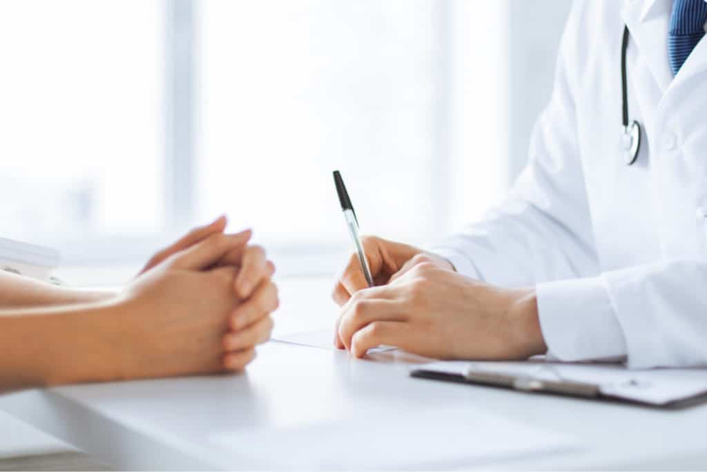 Doctor with stethoscope writing notes during a patient consultation at a medical office desk