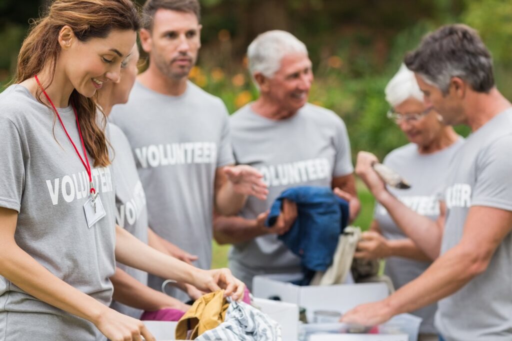 Group of community volunteers in gray t-shirts sorting donated clothing at an outdoor charity drive event