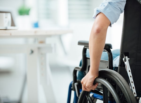 Person using a wheelchair in an office setting, gripping the wheel while navigating near a desk
