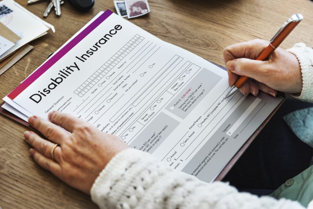 Person filling out a disability insurance application form with a pen on a wooden desk
