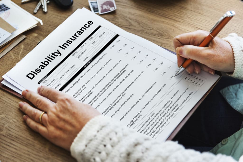 Person completing a disability insurance claim form on a clipboard with a pen at a desk