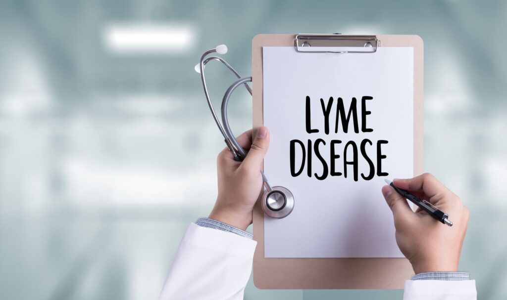 Doctor holding a clipboard with "Lyme Disease" written on it and a stethoscope in a medical setting
