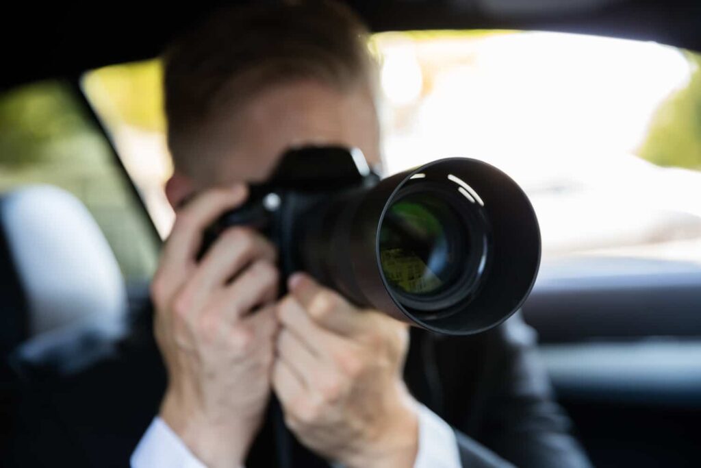 Private investigator sitting inside a vehicle using a telephoto lens camera to conduct covert surveillance
