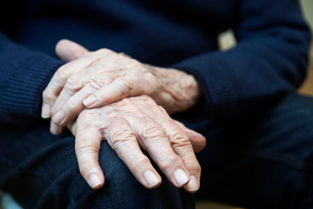 Elderly person's folded hands resting on lap, showing aged skin and visible veins, wearing a dark navy sweater