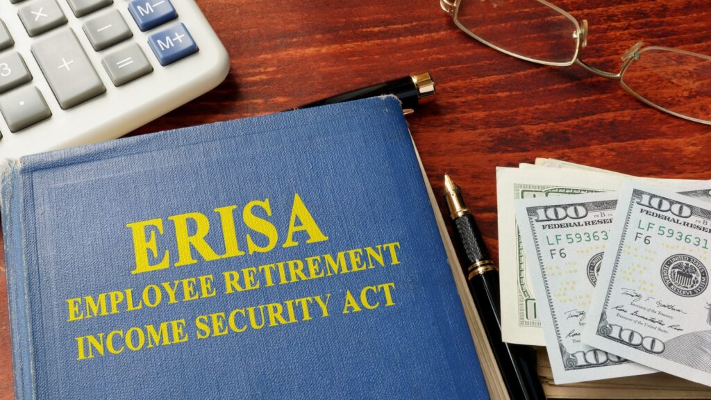 ERISA Employee Retirement Income Security Act book on a desk with $100 bills, a pen, calculator, and reading glasses